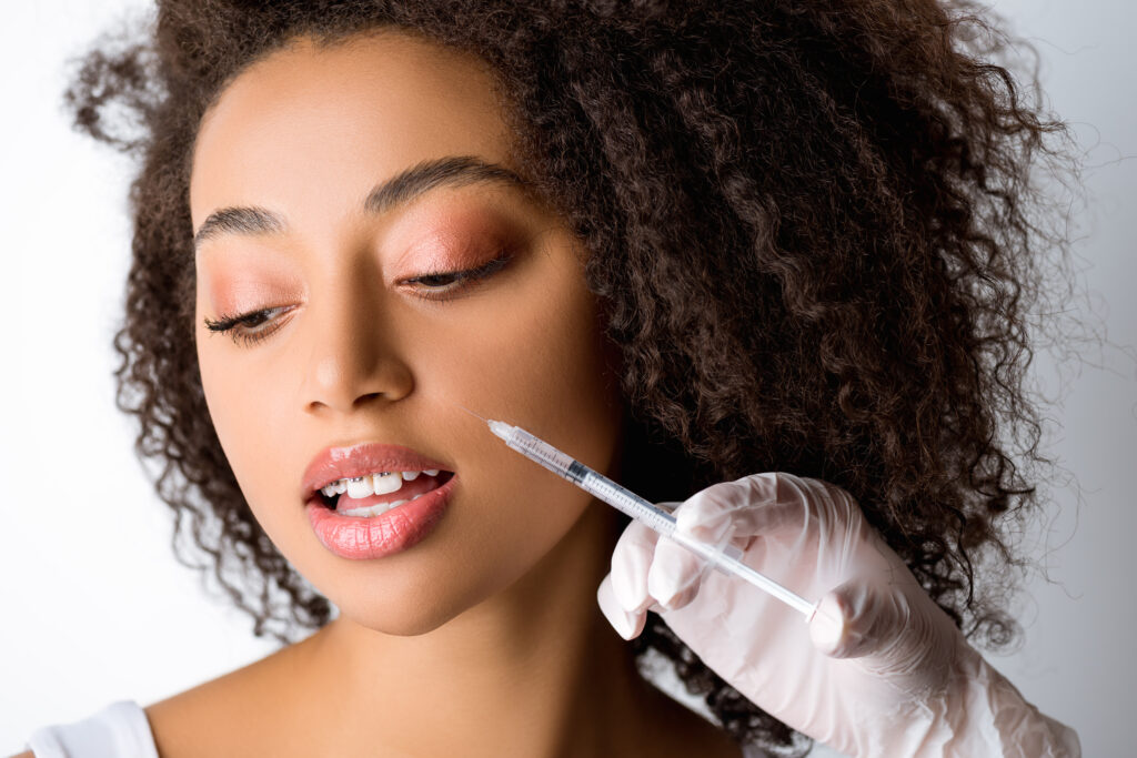 beautiful young african american woman making beauty injection, isolated on grey