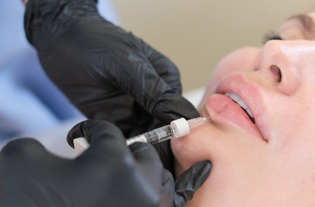 A cosmetologist carefully injects a client's lips. Enhancements come with both benefits and risks