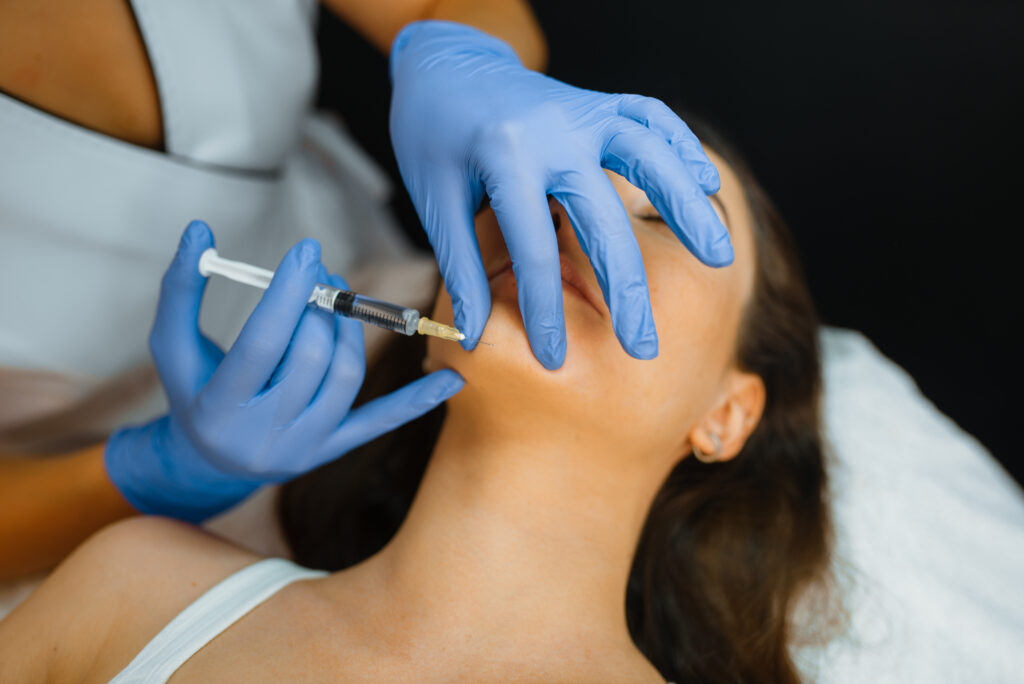 Cosmetician in gloves gives chin botox injection to female patient on treatment table. Rejuvenation procedure in beautician salon. Doctor with syringe and woman, cosmetic surgery against wrinkles